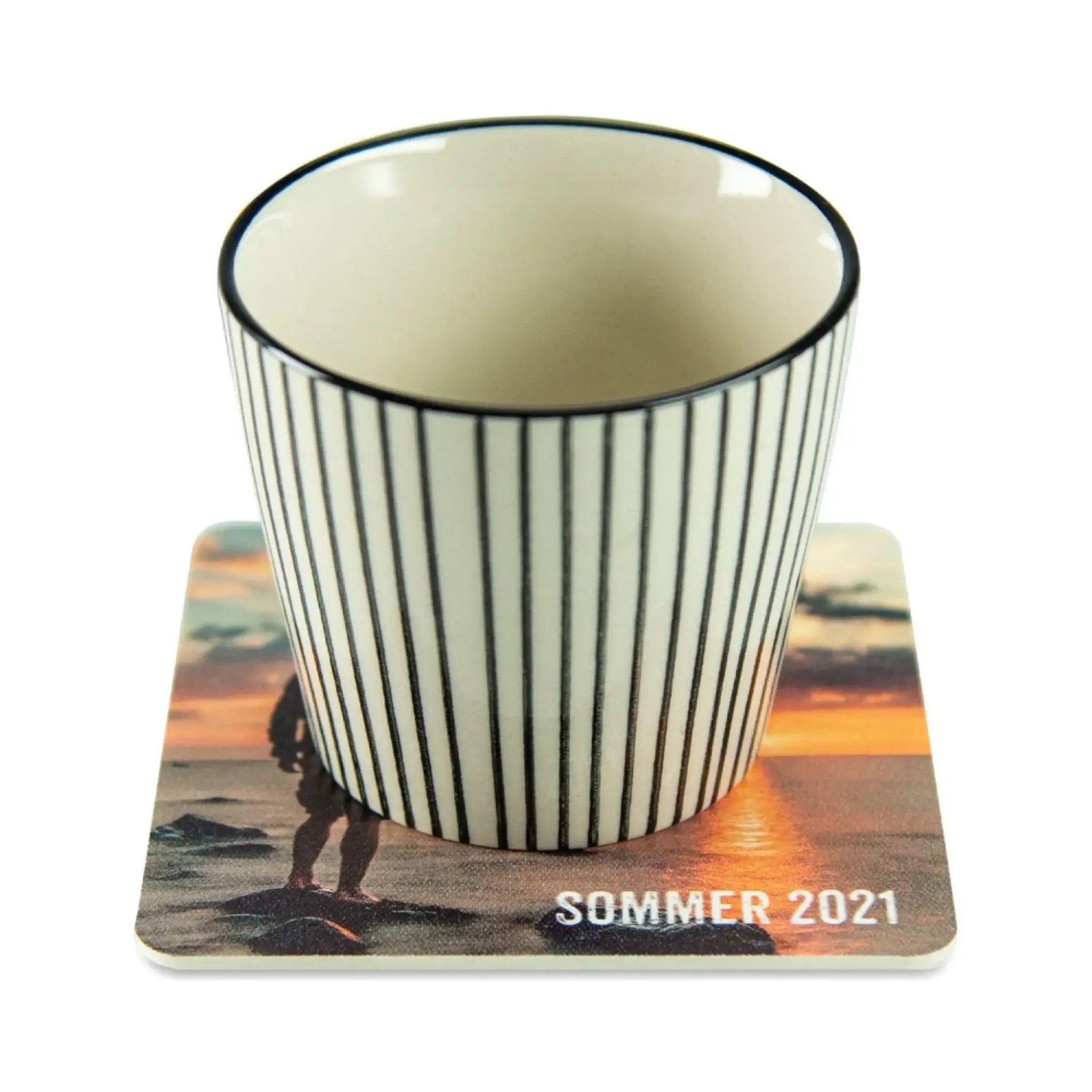 Eine weiße keramik espresso tasse mit schwarzen streifen und schwarzem rand auf coaster mit strand sonnenuntergang