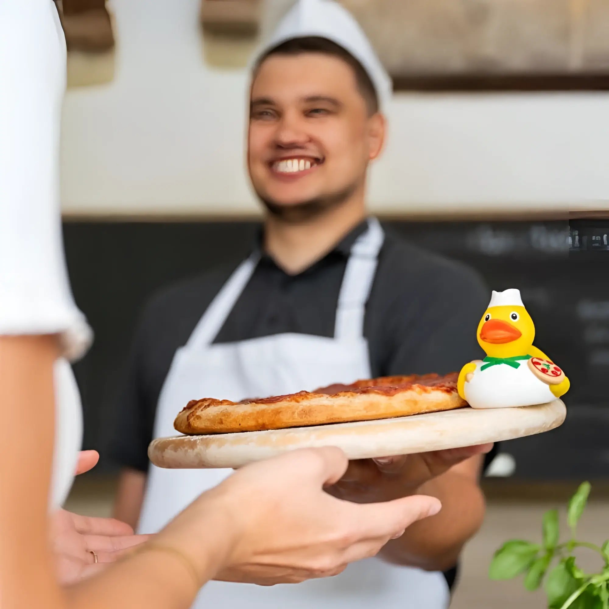 Eine gelbe badeente pizzabĂ€cker mit mini kochmĂŒtze und pizza sitzt auf rustikalem holzbrett, perfekt als dankeschön