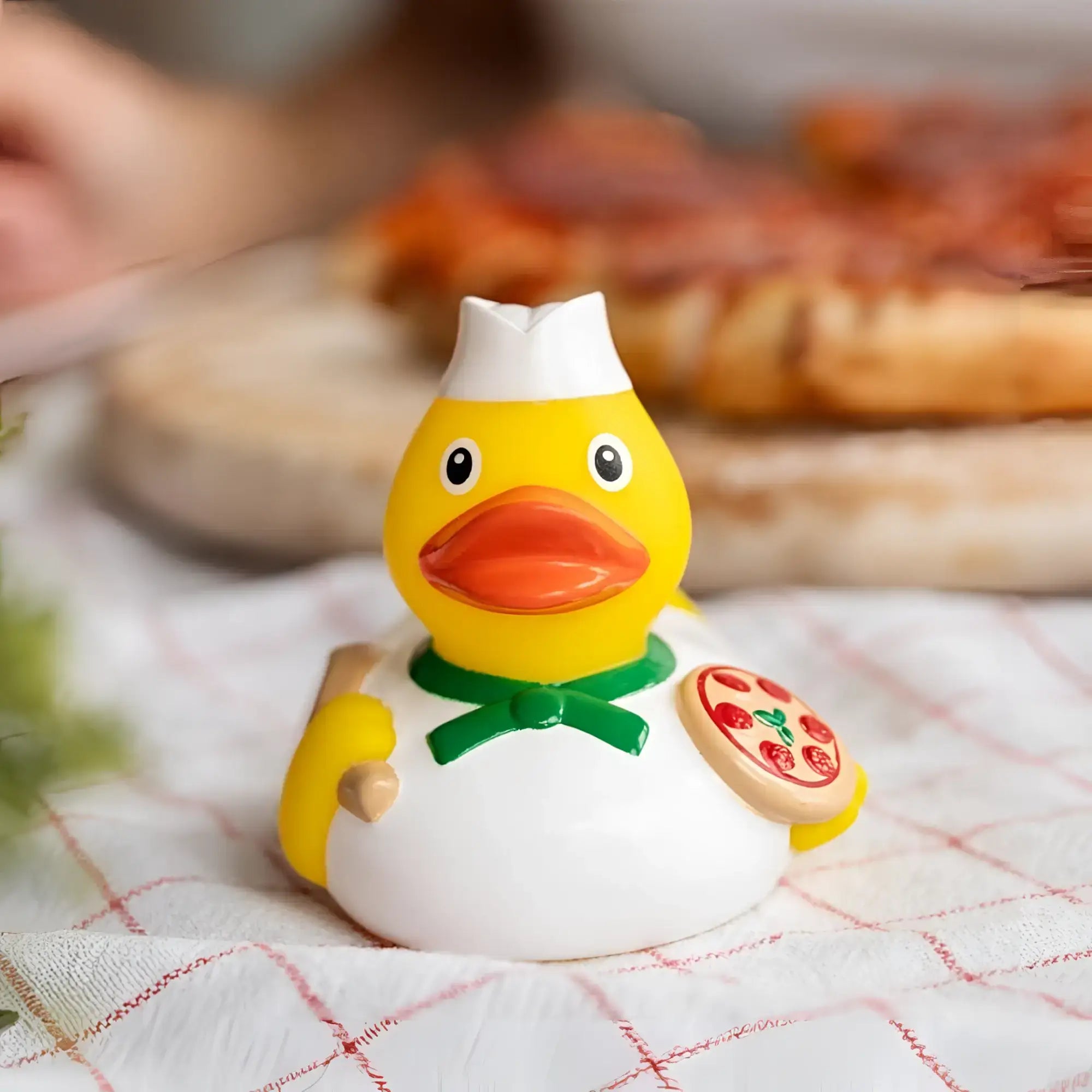 Gelbe badeente pizzabäcker mit weißer kochmütze und grünem fliegenhalter hält pizzastück mit pepperoni