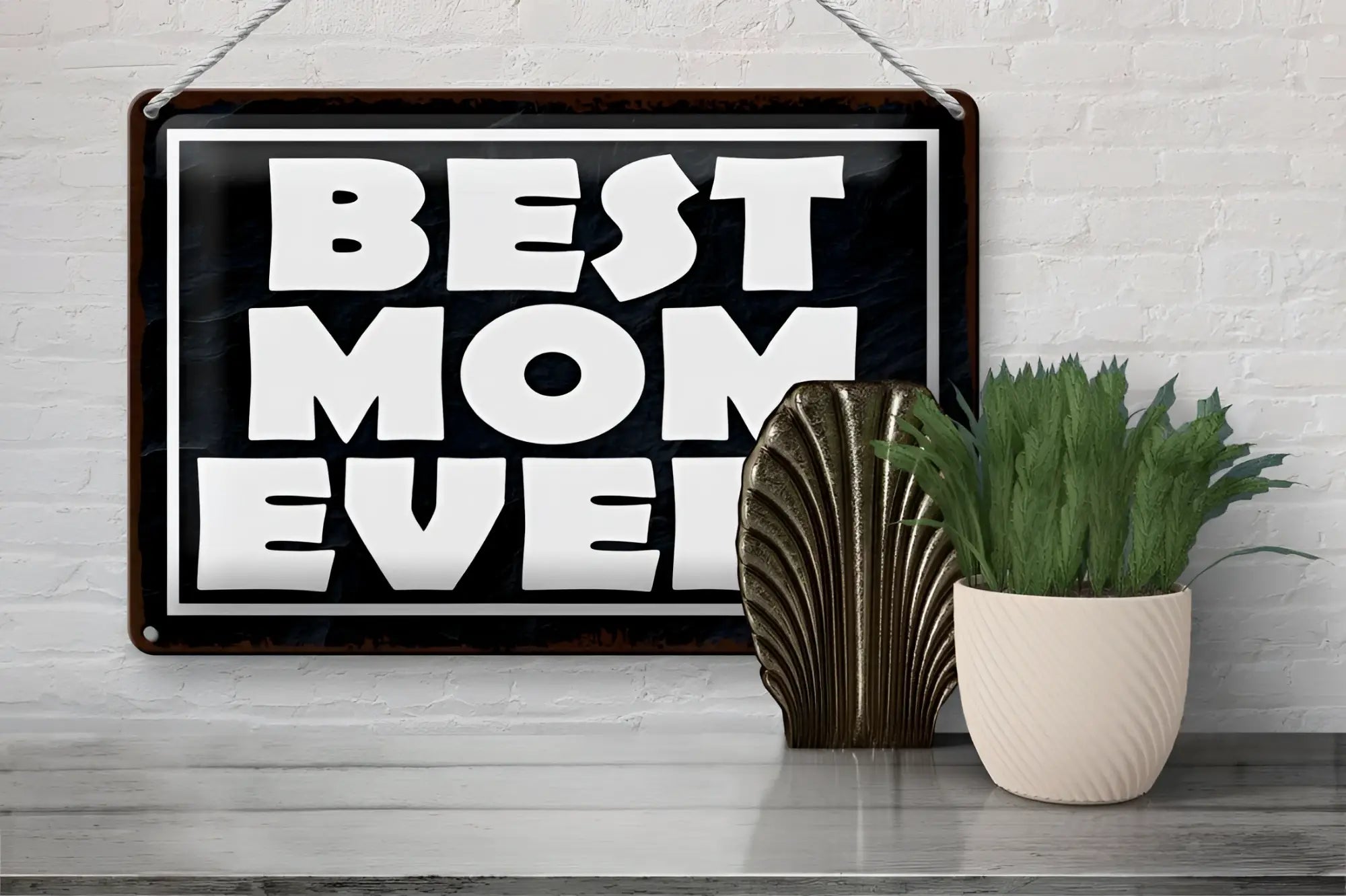 Schwarzes blechschild best mom ever mit weißer schrift und dunklem holzrahmen zum aufhängen an weißer ziegelwand