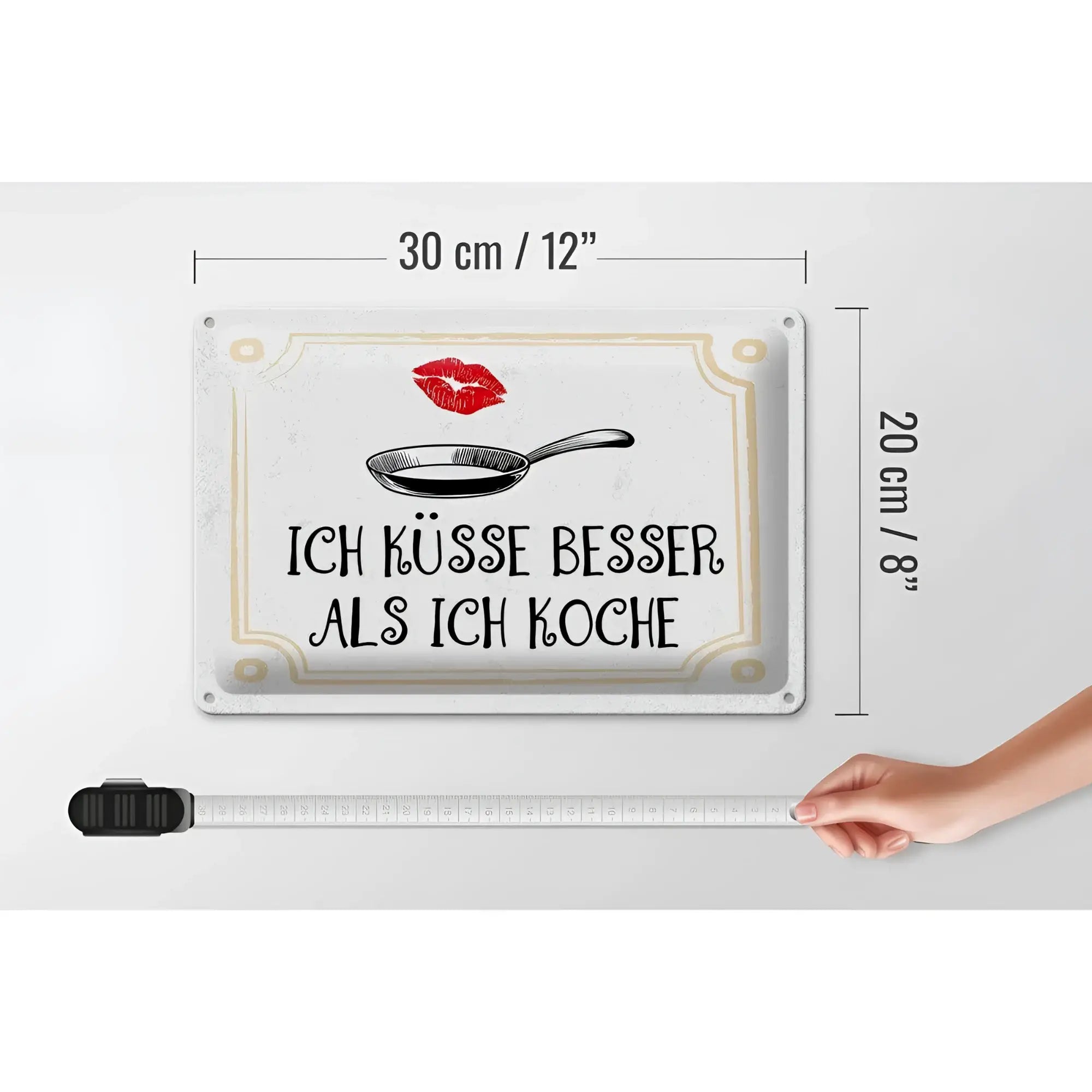 Weißes rechteckiges blechschild mit spruch ich küsse besser als ich koche in schwarz, pfannenillustration und goldrand