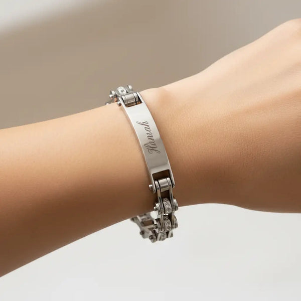 Ein elegentes Armband in silbernem Ton mit einer zentralen gravierten Platte, die den Namen „hannah“ in geschwungener Kalligrafieschrift zeigt, akzentuiert durch kleine eingelassene Steine entlang seiner Kettenglieder.