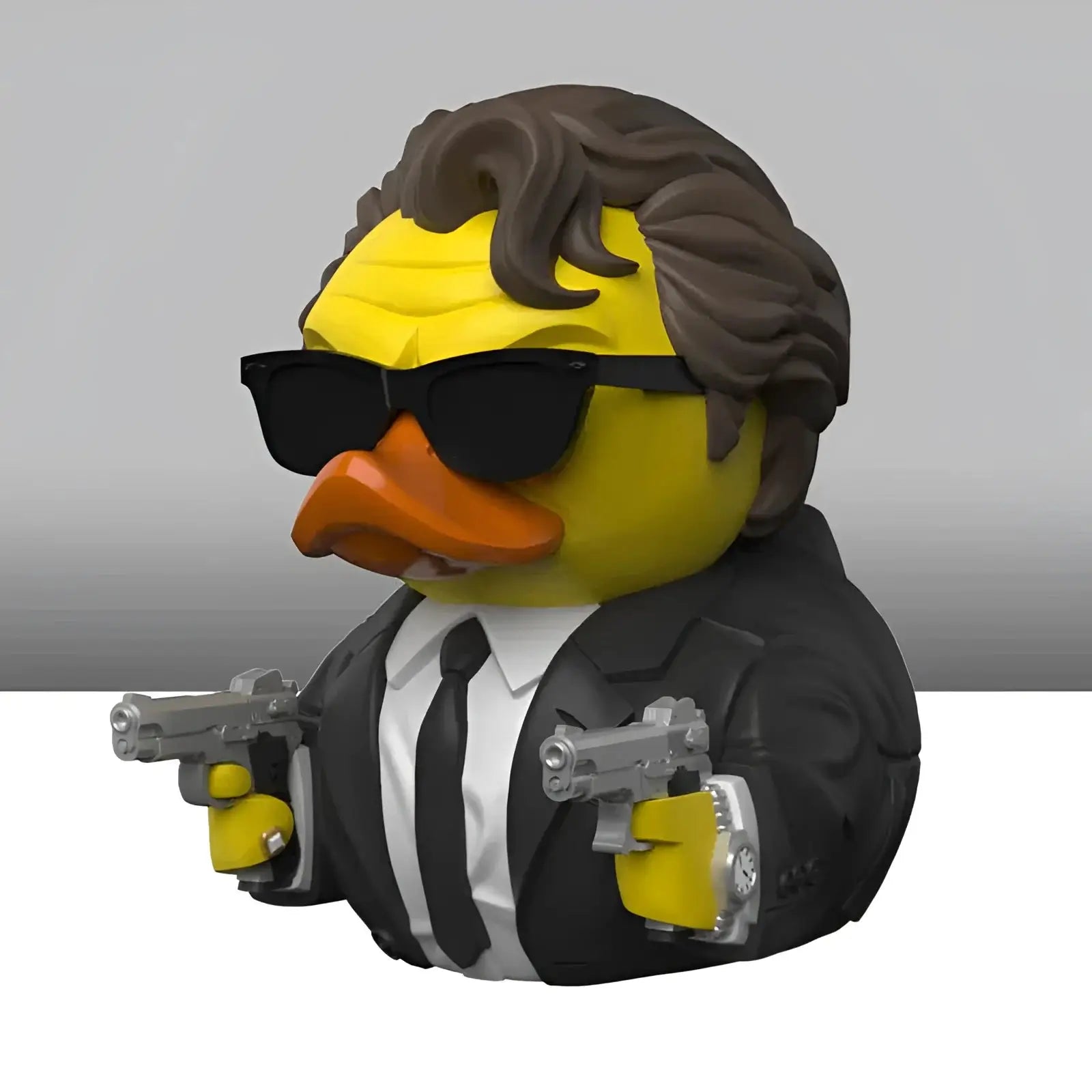 Gelbe gummiente mit braunen locken schwarzen sonnenscheinern und schwarzem anzug hält zwei silberne pistolen im geschenkset reservoir dogs tubbz badeenten