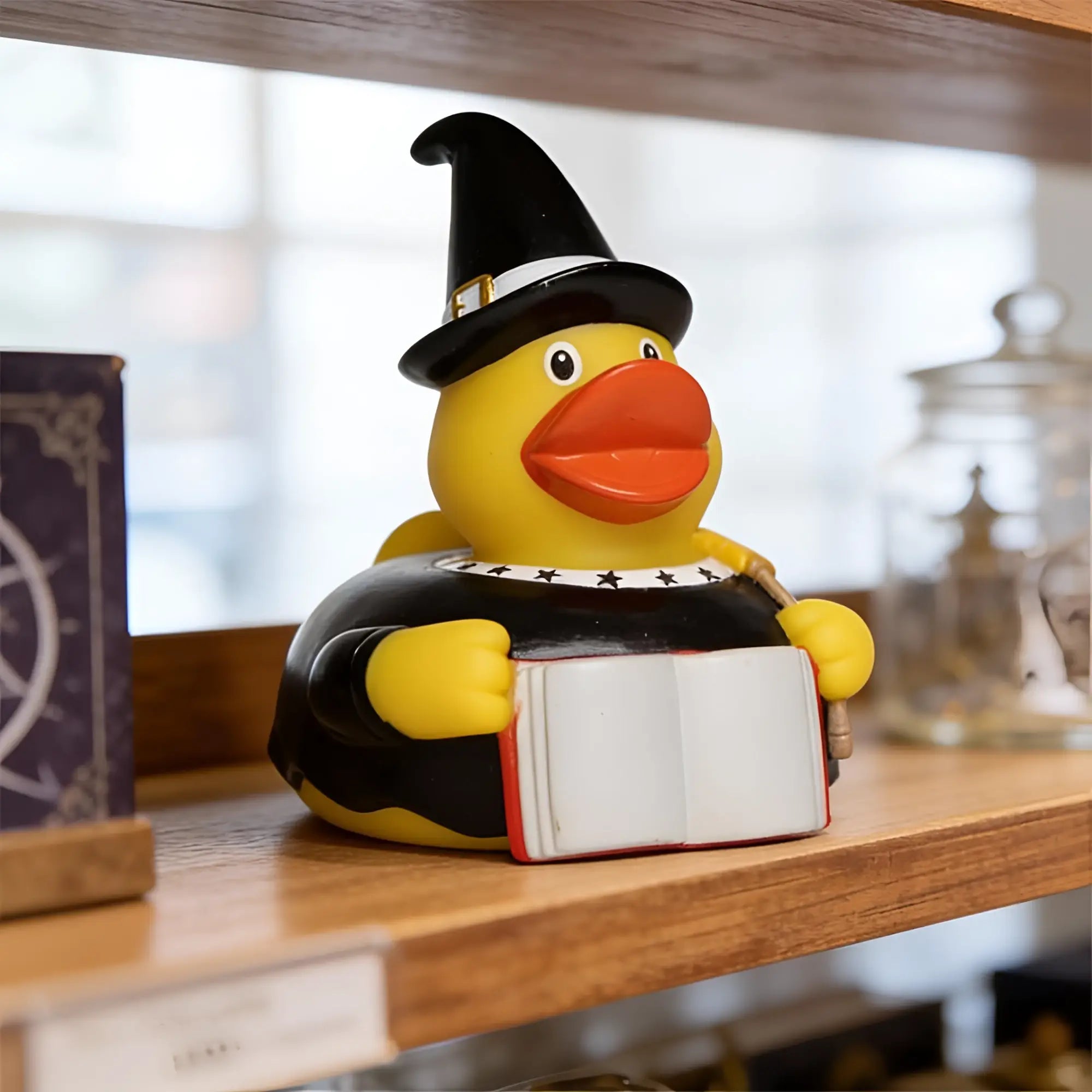 Gelbe quietsche-ente als zauberer mit schwarzem hut und robe hält buch badeente mit quietschfunktion