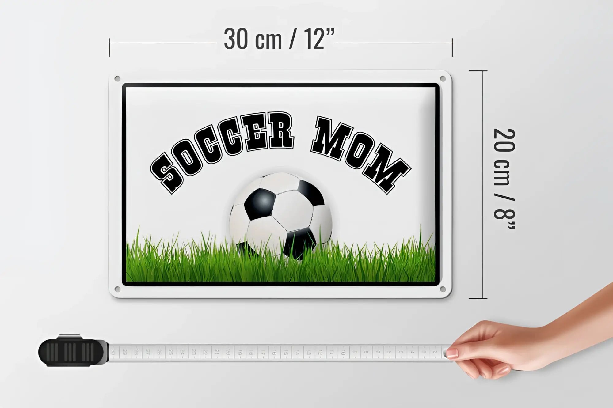 Weißes rechteckiges blechschild 20x30cm mit schwarzem soccer mom text und fußball auf grünem gras