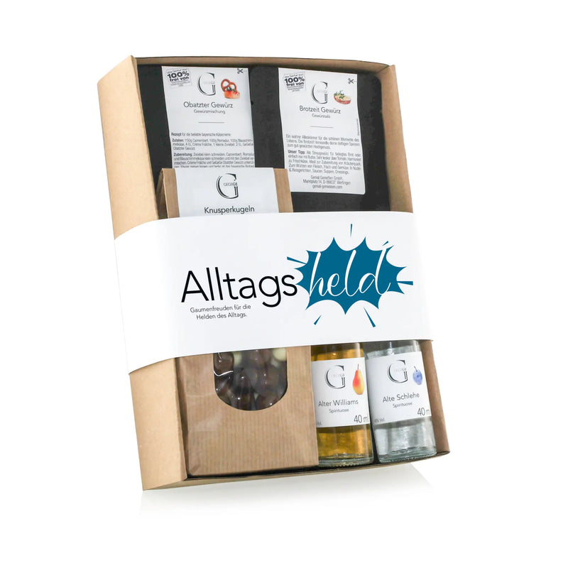 Ein beige geschenkbox aus karton mit einem weißen wrapband und alltagsheld logo gefüllt mit deutschen snacks und likörflaschen