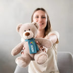 Weiches taupe plüschtier bär nanna mit teal schal und buntem logo stofftier teddy fürs kuscheln