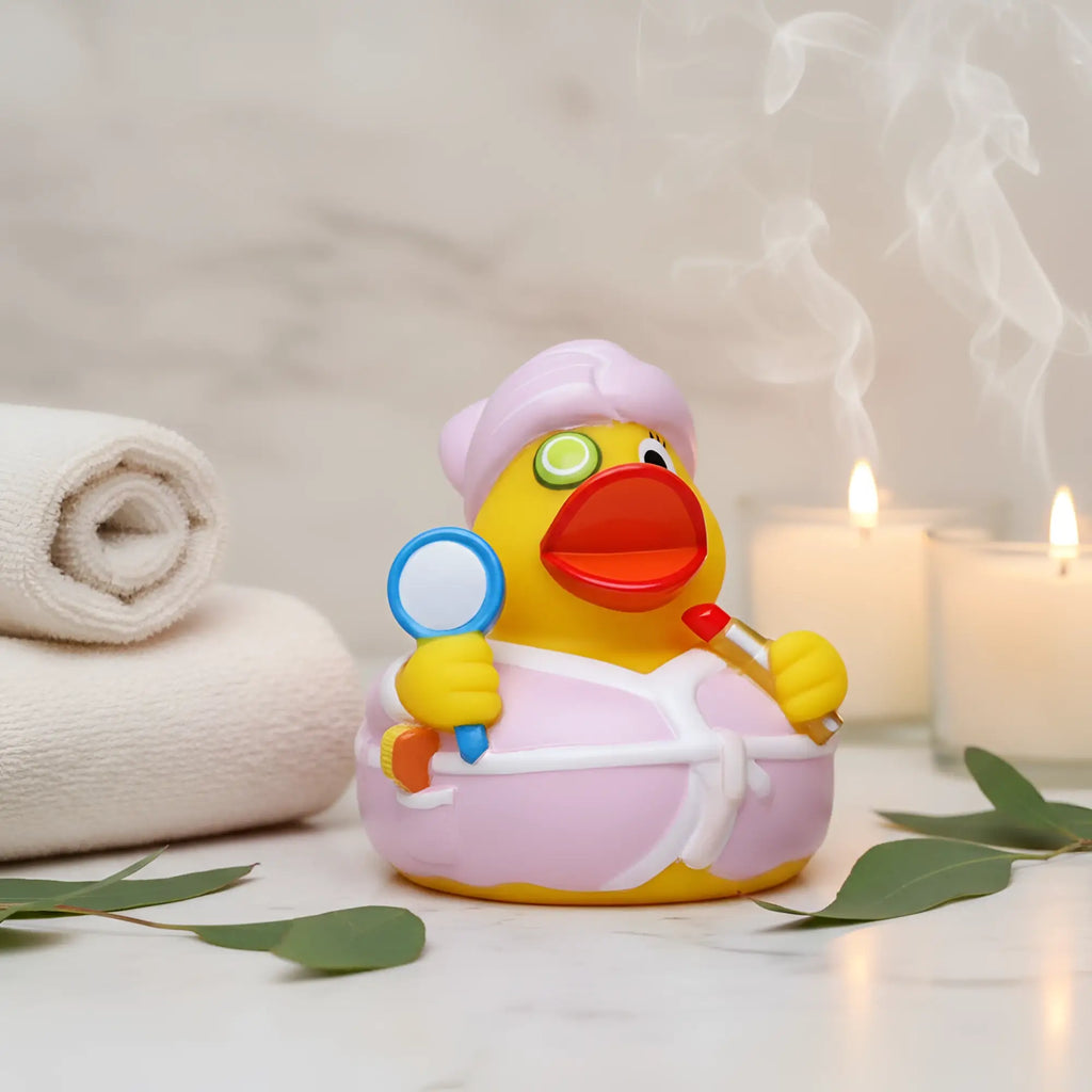 Eine gelbe quietsche-ente mit rosa bademantel und duschkappe hält einen spiegel und roten lippenstift