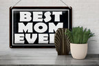 Schwarzes blechschild best mom ever mit weißer schrift und dunklem holzrahmen zum aufhängen an weißer ziegelwand