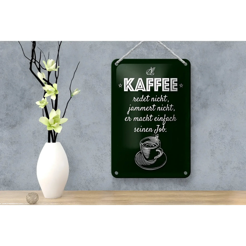 Dunkelgrünes rechteckiges blechschild mit weiß graviertem spruch kaffe jammert nicht job und kaffeeillustration am seil hängend