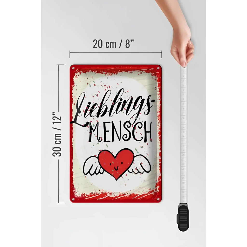 Rotes blechschild mit weißem shabby hintergrund und schwarzem lieblingsmensch schriftzug über lächelndem herz mit flügeln