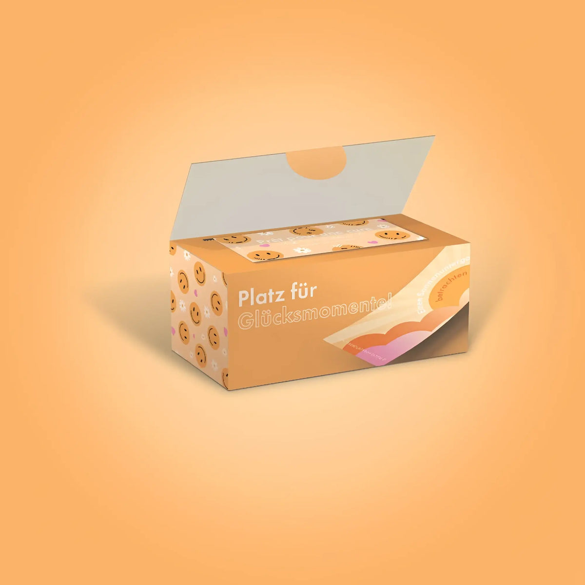 Eine orange kartonbox mit lächelnden keksillustrationen und dem spruch platz für glücksmoment für das kartenspiel challenge-box 30 glücks herausforderungen deutsche version