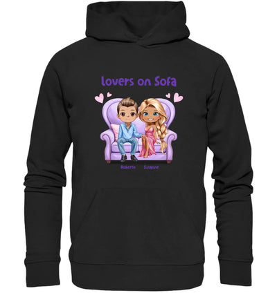 Schwarzer hoodie mit buntem cartoon von zwei figuren auf lila sofa und text lovers on sofa personalisierte figuren