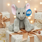 Aweicher grauer plüschelfant mit rosa ohren und schwarzen knopfaugen sitzt auf einem geschenkbox
