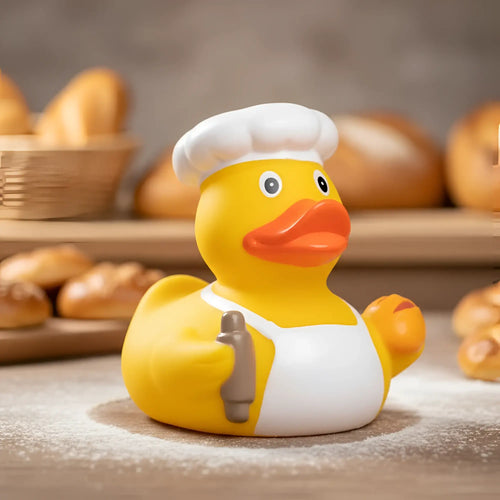 Gelbe quietsche-ente als bäcker mit weißer mütze und schürze hält braune schokosoße flasche für badeente spaß