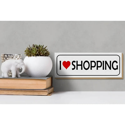 Weißes rechteckiges holzschild mit schwarzem rahmen und dem spruch i herz shopping in schwarzer schrift mit rotem herz