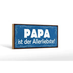 Blaues rechteckiges holzschild mit weißem text papa ist der allerliebste und dekorativen wirbeln am rand