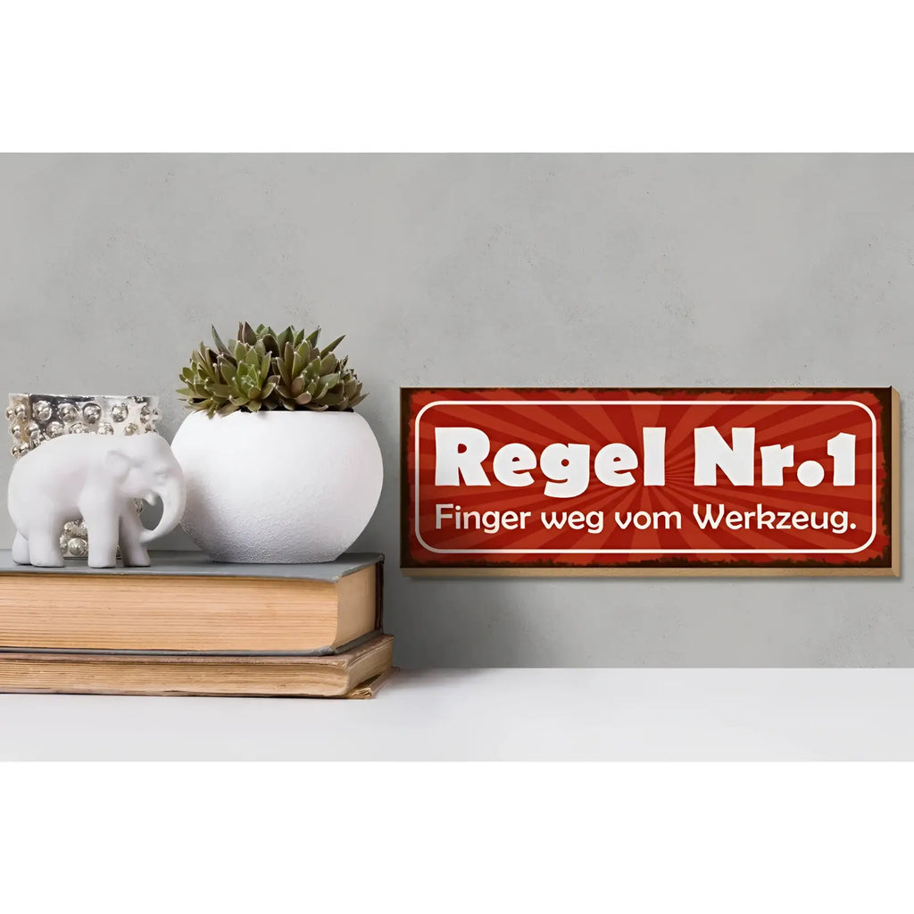 Rotes holzschild 27x10cm mit weißem text regel nr 1 finger weg vom werkzeug und sonnenstrahlenmuster