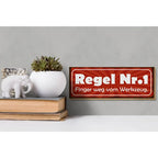 Rotes holzschild 27x10cm mit weißem text regel nr 1 finger weg vom werkzeug und sonnenstrahlenmuster