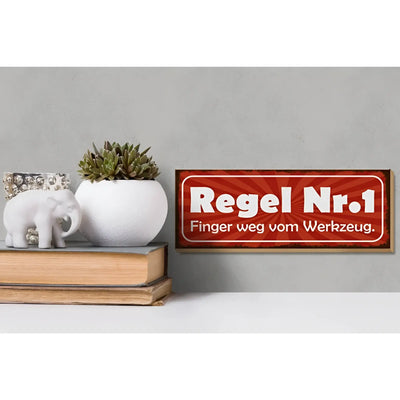 Rotes holzschild 27x10cm mit weißem text regel nr 1 finger weg vom werkzeug und sonnenstrahlenmuster