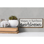 Weißes keramikwandschild mit schwarzem kursivtext wegen reichtum geschlossen und kleiner krone in holzrahmen