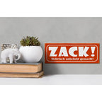 Orange rechteckiges holzschild 27x10cm mit weißem schriftzug zack und kleinem deutschen spruch darunter