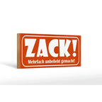 Orange rechteckiges holzschild mit weißem zack schriftzug und kleinerem text darunter 27x10cm