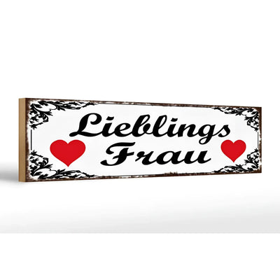Weißes rechteckiges Holzschild mit schwarzem Ornamentrahmen und dem Schriftzug lieblingsfrau zwischen roten Herzen, 46x10cm