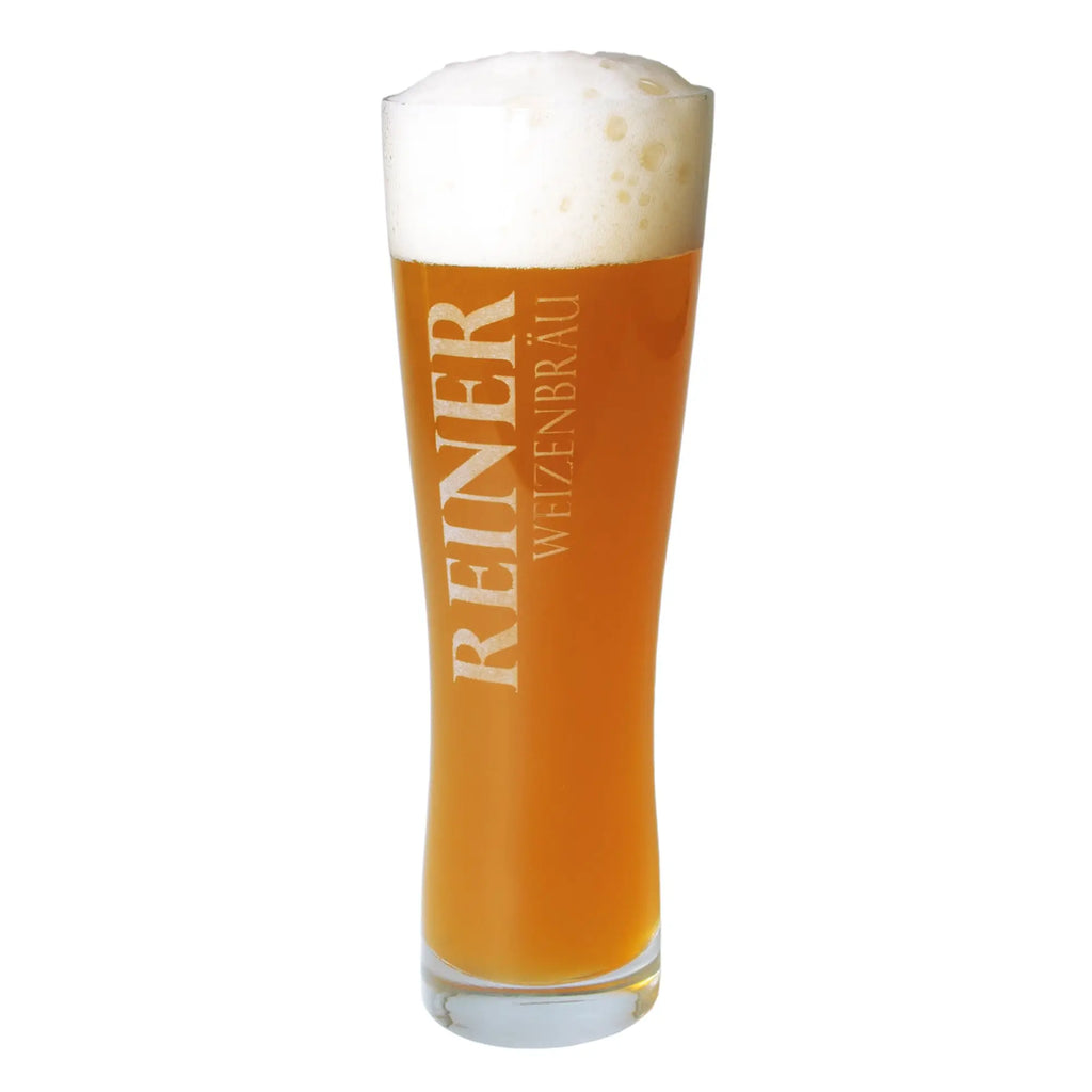 Ein 500 ml weizenbierglas mit der gravur reiner wiesenbräu gefüllt mit bernsteinfarbenem bier und schaumkopf