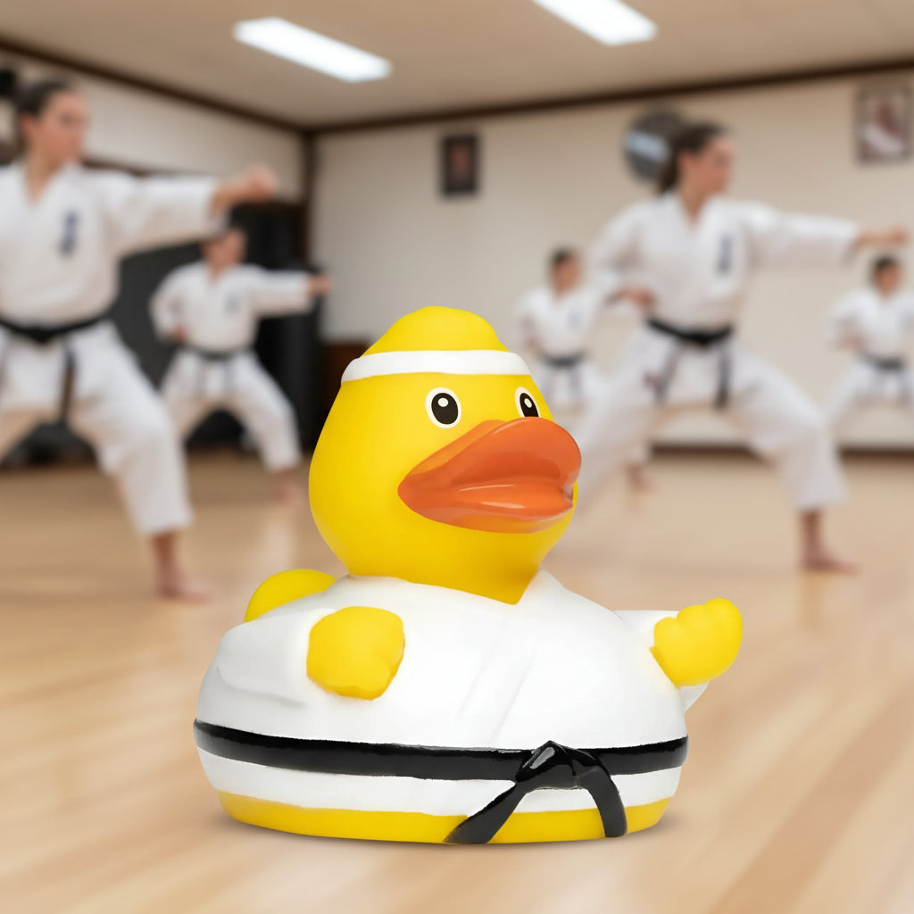 Gelbe quietsche-ente in weißem karate-gi mit schwarzem gürtel und stirnband fürs bad und kampfsportspaß