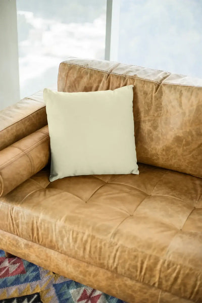 Creamfarbiges viereckiges kissen auf tanfarbenem ledersofa aus der statement collection mit wunschtext