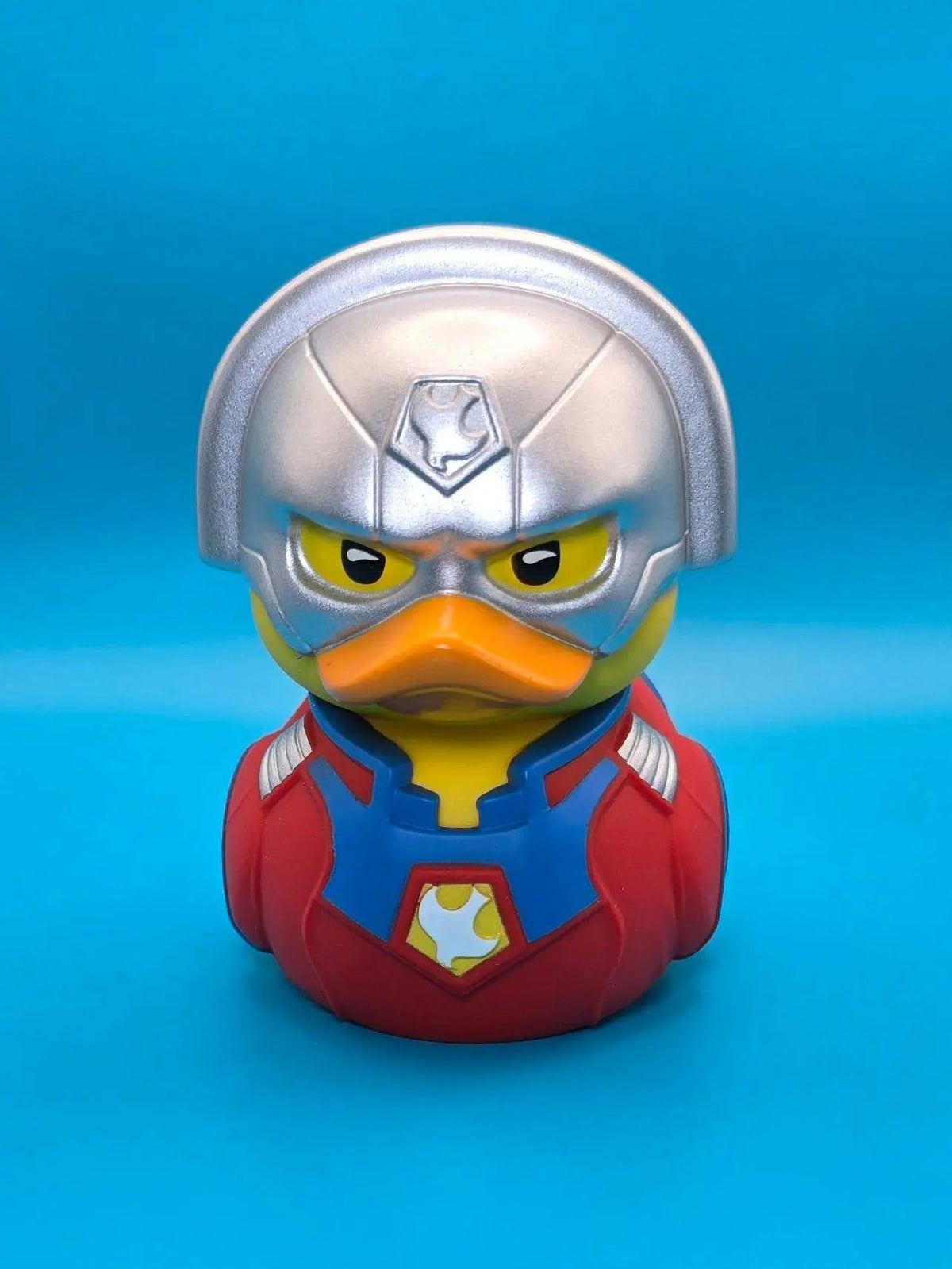 Eine silberne helmente figur in einem rot-blauen superheldenanzug mit gelbem emblem aus pvc von tubbz peacemaker