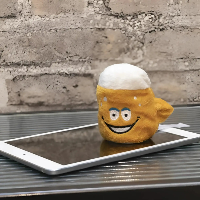 Ein plüschiger, goldgelber schmoozies displayreiniger bier in form eines bierkrugs mit weißem schaum und stickerei liegt auf einem tablet