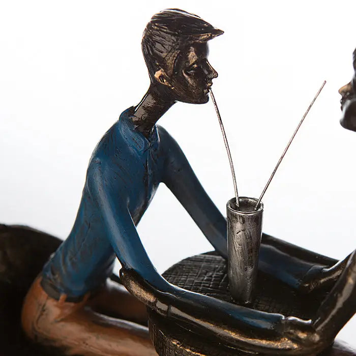 Bronze farbene skulptur eines mannes in blauer kleidung der aus einem silbernen becher mit zwei strohhalmen trinkt kunstharz