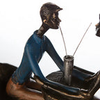 Bronze farbene skulptur eines mannes in blauer kleidung der aus einem silbernen becher mit zwei strohhalmen trinkt kunstharz