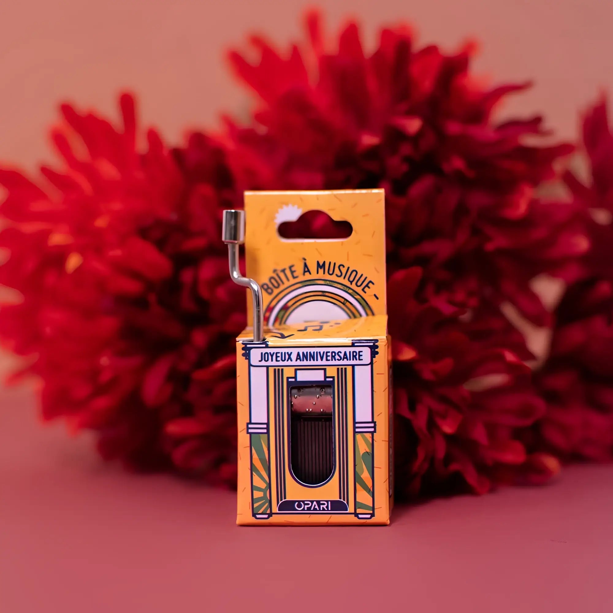 Miniatur gelbe kartonbox mit einer vintage spieluhr mit silbernem kurbelgriff und schwarzem inneren von opari fürs jubiläum