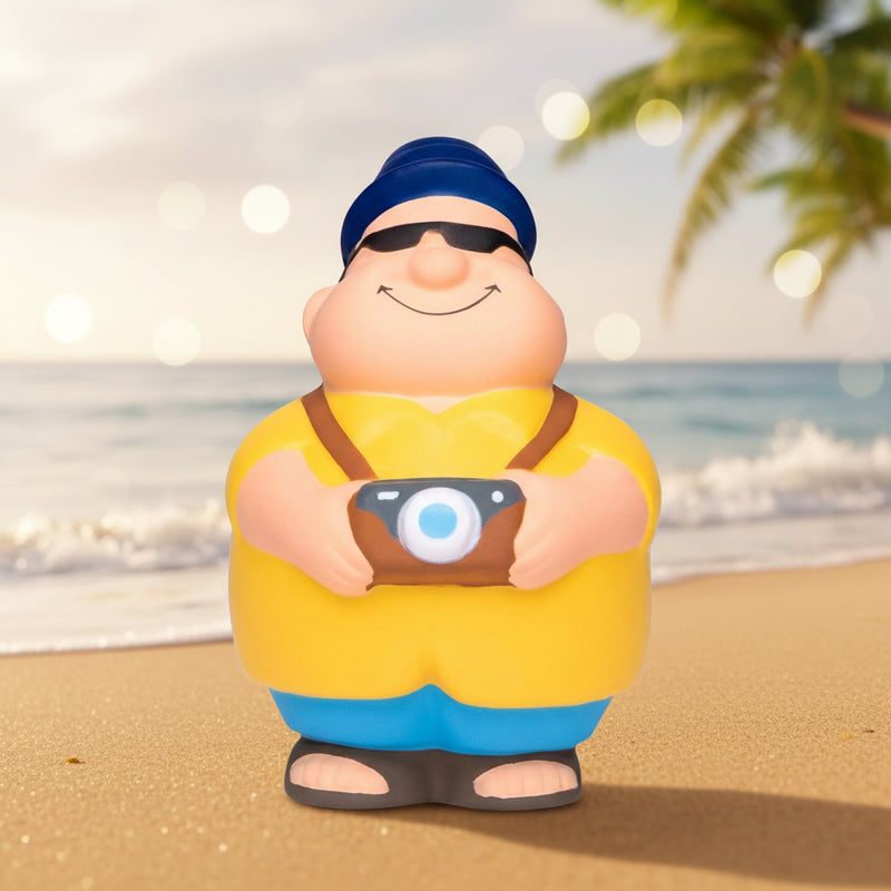 Gelbe und blaue anti-stress-quetsch-figur touri bert mit kamera trägt mütze sonnenbrille und sandalen