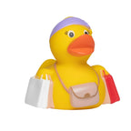 Gelbe badeente mit lila stirnband trägt einkaufstaschen und beige umhängetasche aus quetschfigur geschenkseturlaub