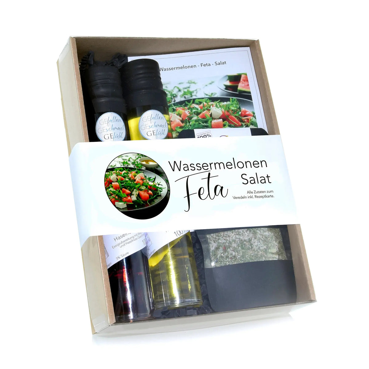 Präsentkorb mit zwei schwarzkappigen glasflaschen für öl und essig, kräuterbeutel und rezeptkarten für wassermelonen feta salat
