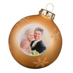 Weihnachtskugel mit foto in gold und glitzernden schneeflocken zeigt ein lächelndes brautpaar im hochzeitsoutfit